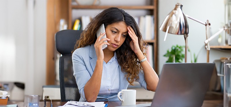 Frustrated woman holding a smartphone and looking at her laptop
