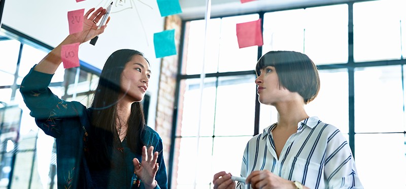 Two women looking at post-it notes on a board