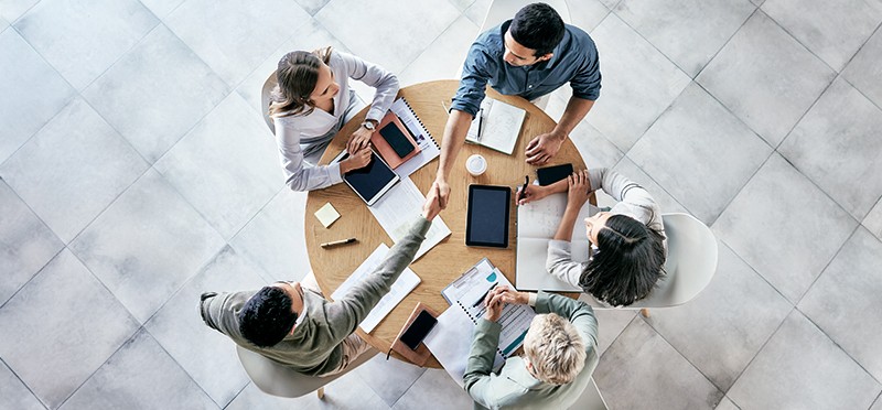 A group of coworkers sitting at a table, two of whom are shaking hands