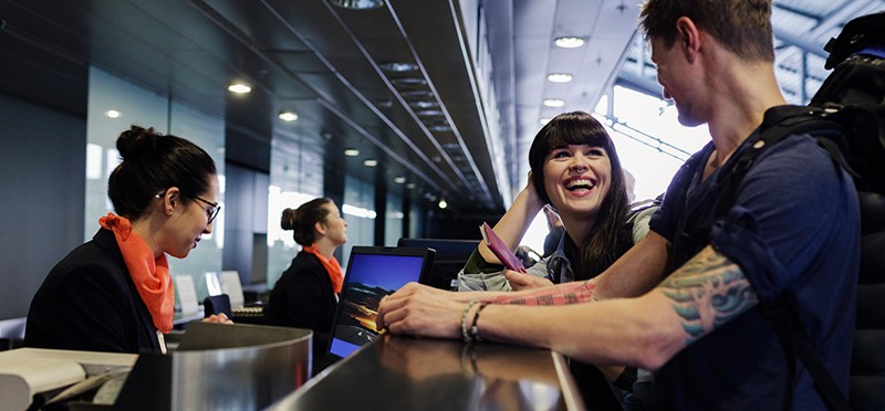 Woman and man at a counter in an airport, with a woman who works there looking at a computer.