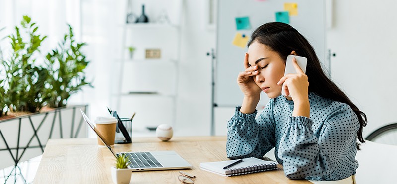 Woman on cellphone, sitting at laptop, looking frustrated