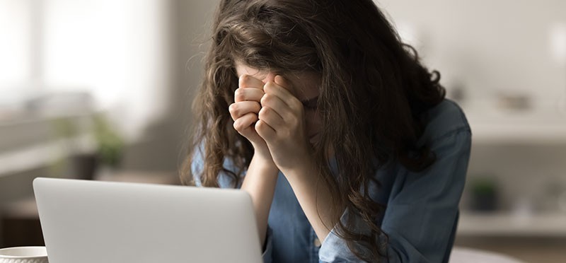 Frustrated woman with her head in her hands, sitting in front of a laptop