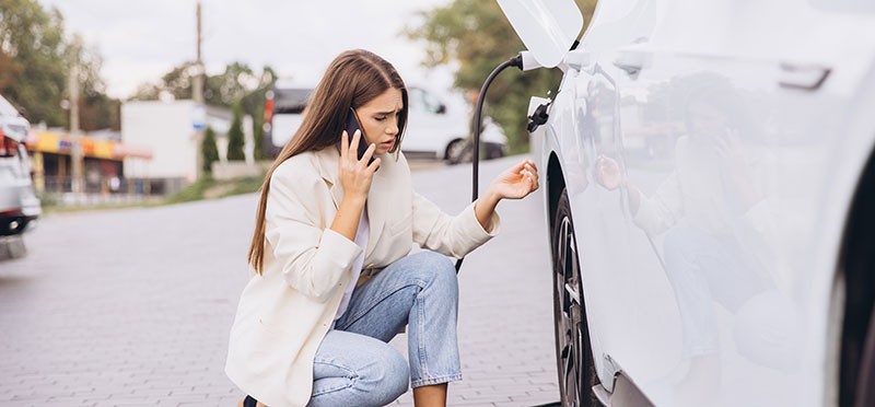 Woman kneeling near an electric car that's charging