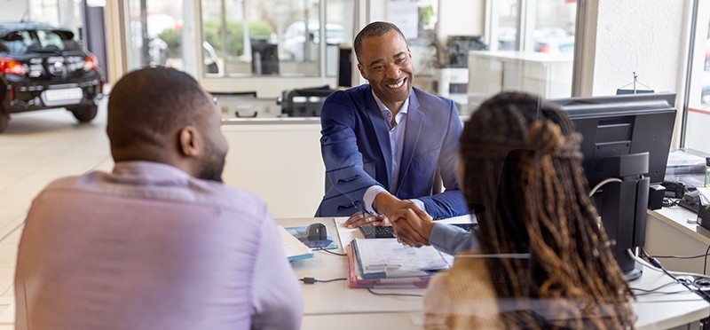 Couple sitting across a deck from a salesman in a car dealership 