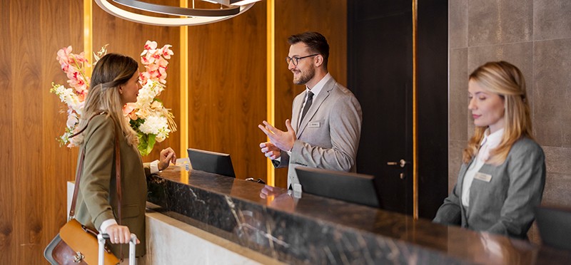 Woman checking in to a hotel with two hotel employees at the front desk 