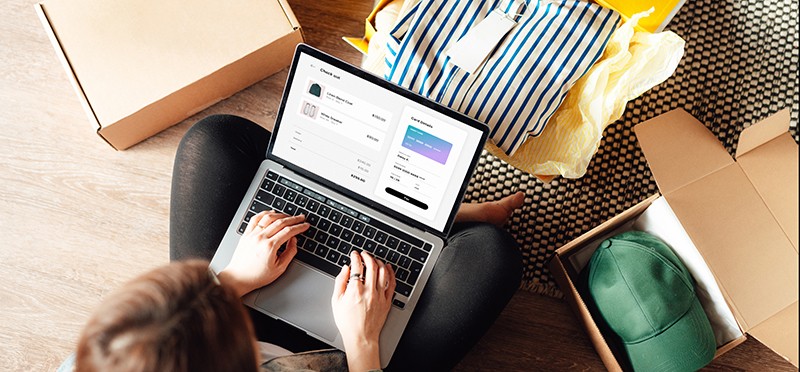 Woman looking at at online shopping site on a laptop, with a shirt in a box in front of her