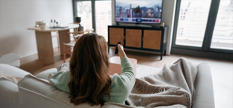 Woman sitting on a couch, pointing a remote at a television 