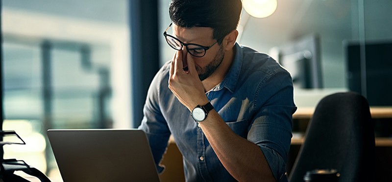 A man sitting at a laptop looking frustrated 
