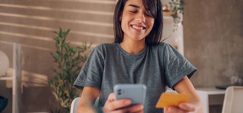 Woman smiling, holding a credit card in one hand and a smartphone in the other 