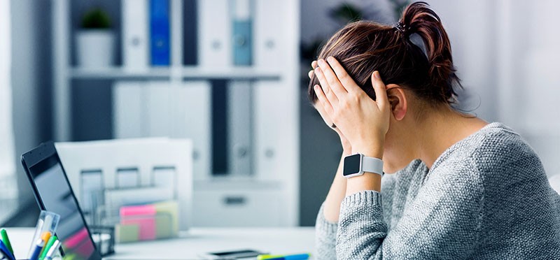 A woman with her head in her hands, looking frustrated, in front of a laptop