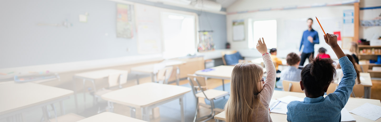 Children in a classroom holding up their hands to be called on