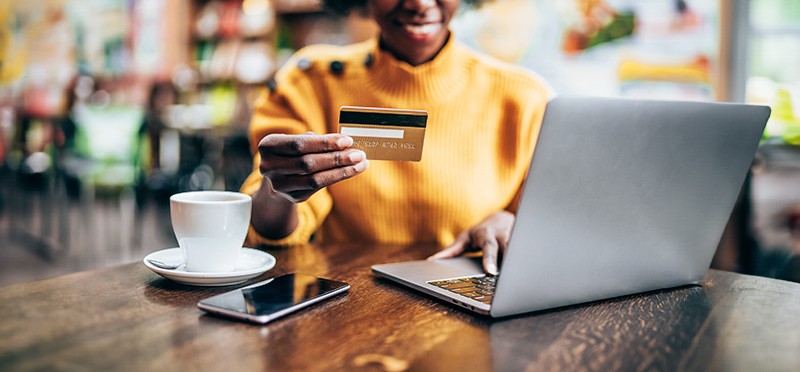 Woman on a laptop holding a credit car in a coffee shop