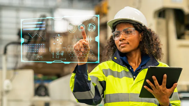 Woman wearing vest and hardhat looking at a digitized computer screen 