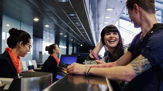 Woman and man at a counter in an airport, with a woman who works there looking at a computer.