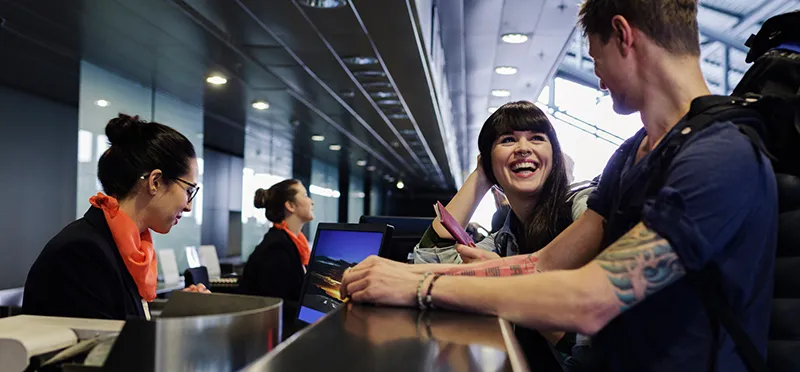 Woman and man at a counter in an airport, with a woman who works there looking at a computer.