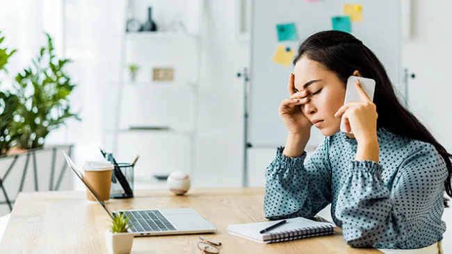 Woman on cellphone, sitting at laptop, looking frustrated