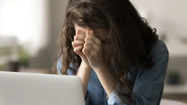 Frustrated woman with her head in her hands, sitting in front of a laptop