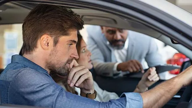 Man and woman sitting in a can speaking to a man who's leaning in the front window.