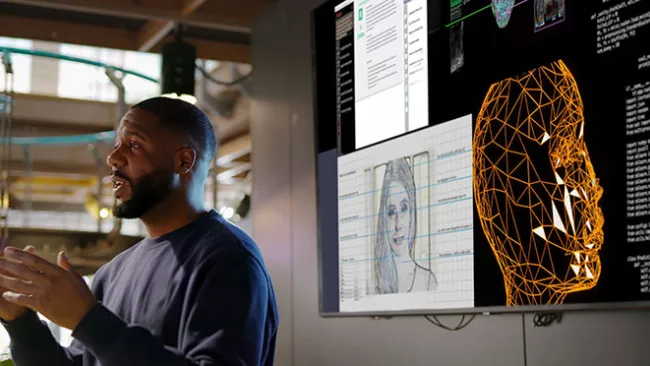 Man standing in front of computer screens that show digital/futuristic images of people