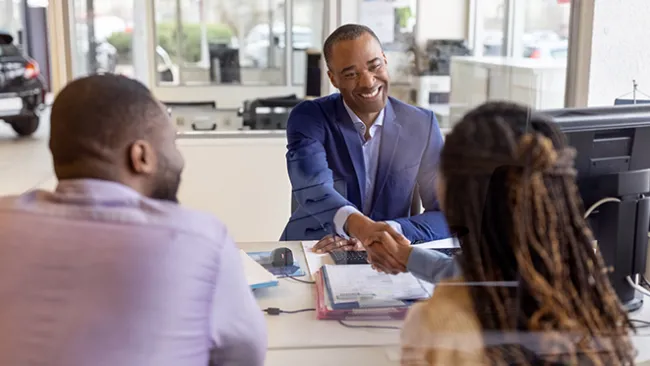 Couple sitting across a deck from a salesman in a car dealership 