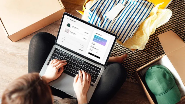 Woman looking at at online shopping site on a laptop, with a shirt in a box in front of her