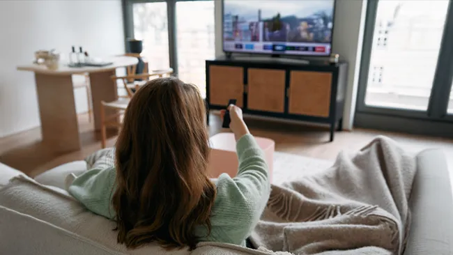 Woman sitting on a couch, pointing a remote at a television 