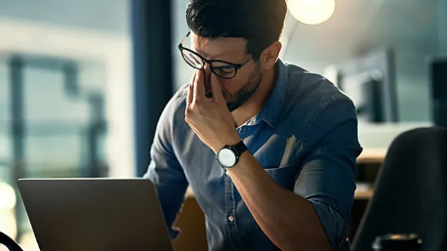 A man sitting at a laptop looking frustrated 