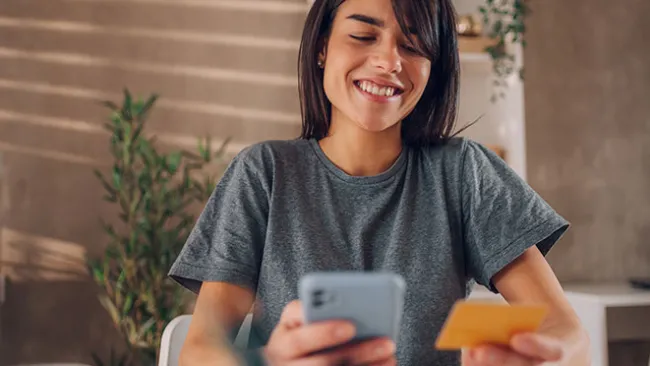 Woman smiling, holding a credit card in one hand and a smartphone in the other 