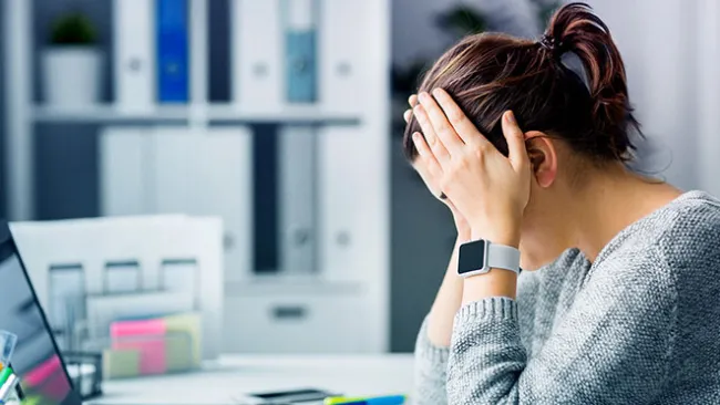 A woman with her head in her hands, looking frustrated, in front of a laptop