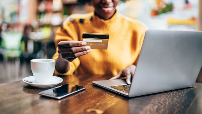 Woman on a laptop holding a credit car in a coffee shop