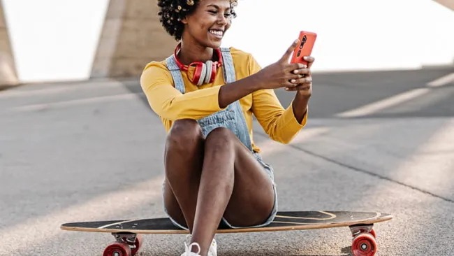 Woman using her phone while sitting on skateboard