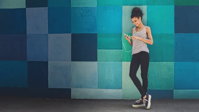 Woman standing against a colorful wall using her phone